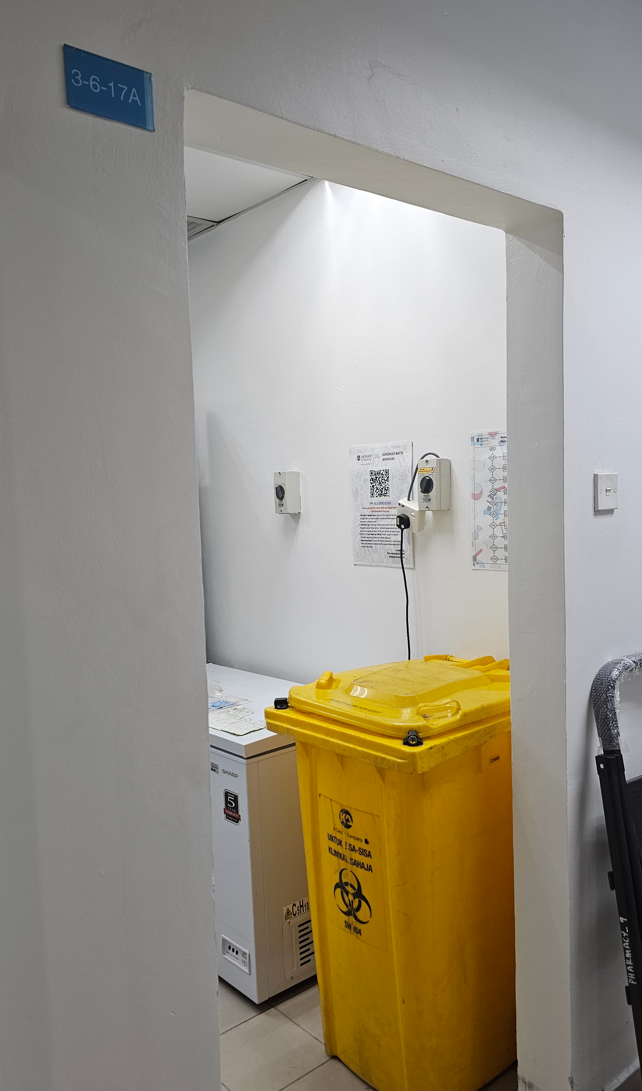 Doorway to room 3-6-17A with the blue room sign, showing the yellow SW 404 clinical waste bin inside beside a freezer